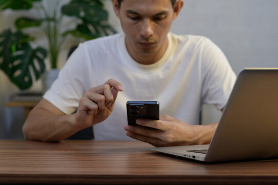 Focused young man using smartphone while sitting at wooden desk