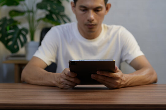 Man Sitting at Table Engaged with Tablet Amidst Indoor Plants