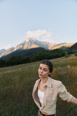 Naklejka premium Woman in casual attire stands in a meadow with distant mountains, showcasing an outdoorsy lifestyle, calm nature, and exploration under soft natural light. Warm glow.