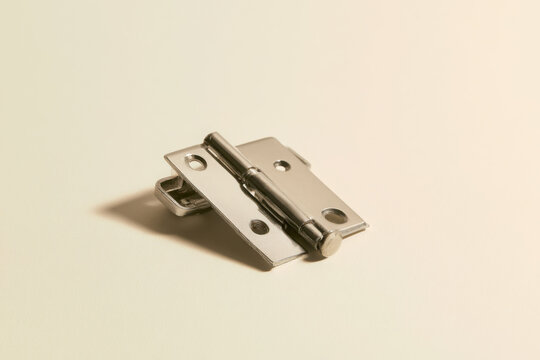 Small metal hinge isolated on a warm cream background with copy space, representing construction hardware, cabinetry, repair and home improvement.