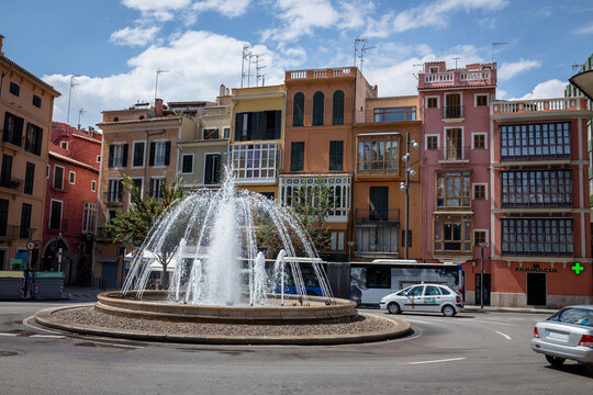 Fountain in center of roundabout surrounded by narrow colorful historic buildings in Mallorca, Spanish urban architecture and city square scene