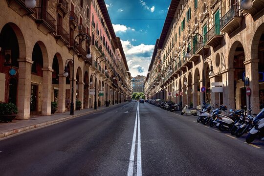 Empty historic street in Mallorca lined with arcaded stone buildings and balconies with parked motorcycles and scooters, Spanish architecture and urban scene