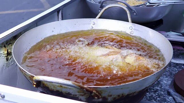 A cook flips a whole pink snapper in bubbling hot oil until crisp. Concept of traditional Asian cooking, fried seafood, street food and local cuisine.
