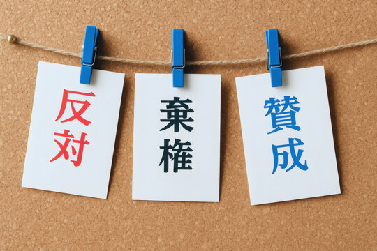 青いクリップで麻ひもに吊るされた「反対」「棄権」「賛成」の文字が書かれた紙がコルクボードの背景に並ぶ