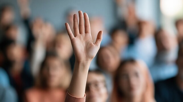 Close-up of a hand raised in a crowd, seeking attention or asking a question during a presentation or meeting