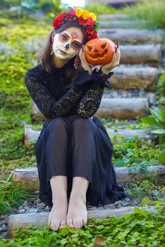 Halloween beauty portrait of woman sitting on a wooden staircase with Halloween pumpkin in hand.