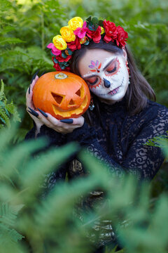 Halloween beauty portrait of female among ferns with Halloween pumpkin in hand. Eyes closed.