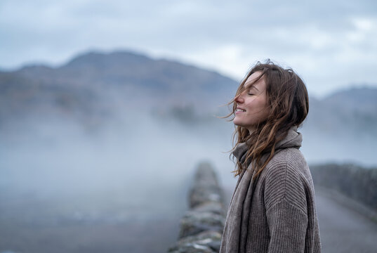 Woman standing from behind gazing misty mountain valley landscape