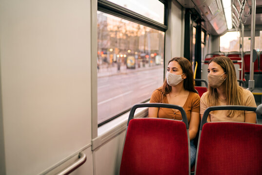 Two women wearing masks on public transport bus looking outside