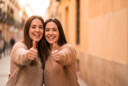 Two young women giving thumbs up on urban street in casual attire
