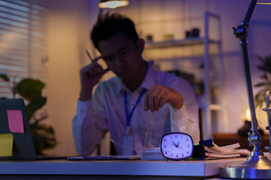 Asian businessman working late at night in office sitting exhausted at desk