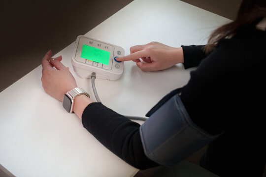 Woman measuring blood pressure using digital monitor at table for cardiovascular health check