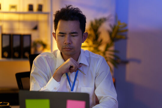 Focused Asian businessman thinking while working late on laptop in office