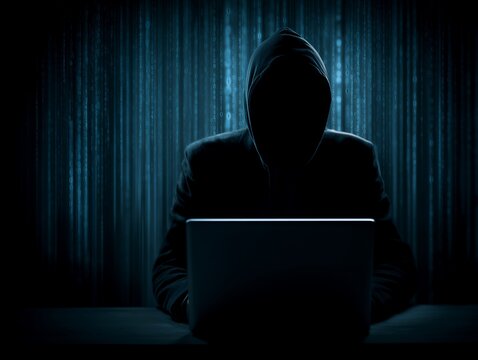 フードを被ったハッカーが暗闇でパソコンを操作するサイバーセキュリティ概念