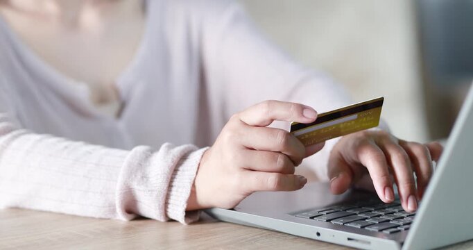 Close-up of a woman holding a credit card while using a laptop for online payment. e-commerce, secure digital transaction, online shopping, fintech, and cashless payment