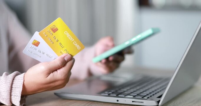 Close-up of a woman holding a credit card while using a laptop for online payment. e-commerce, secure digital transaction, online shopping, fintech, and cashless payment