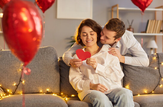 Couple embracing and holding a red heart during Valentine Day celebration at home. Love, affection, and the joy of family holiday and relationships in a warm and romantic domestic setting.