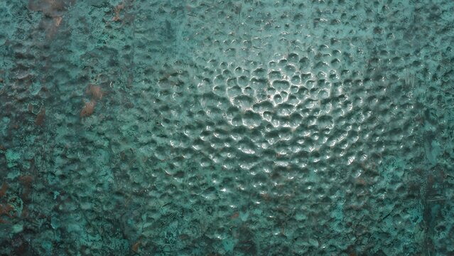 Close-up of textured verdigris copper surface with hammered dimples and weathered patina