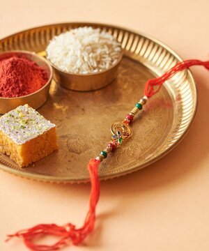 Raksha Bandhan Rakhi with Rice, Kumkum and Traditional Indian Sweets on Brass Plate