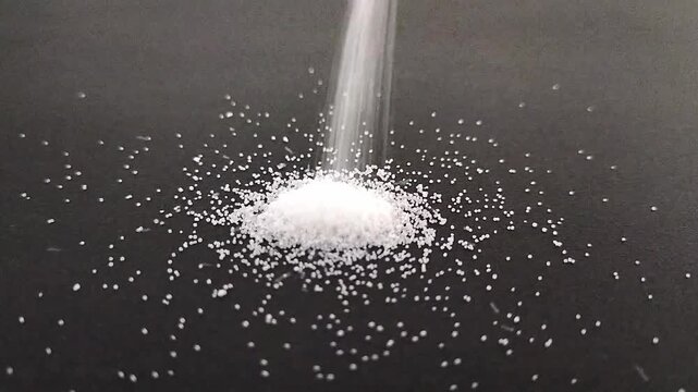 黒背景の上に降り注ぎ高く積み上がる白い塩の粉末マクロ