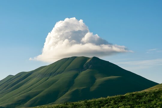 Einzelne wei&szlig;e Wolke schwebt &uuml;ber einem sattgr&uuml;nen Berg unter blauem Himmel