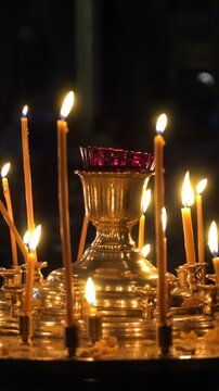 Golden light from numerous thin wax candles flickering in a dark, sacred space, illuminating a large ornate candelabrum during a solemn christian orthodox religious service