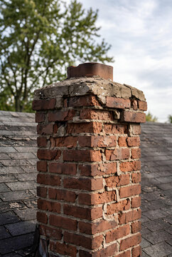 A house chimney with missing mortar and spalling brick at the top