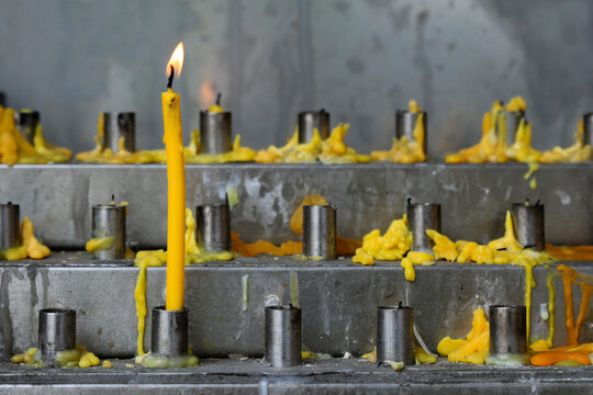 Single Lit Yellow Candle Among Melted Wax Offerings at Buddhist Temple Shrine