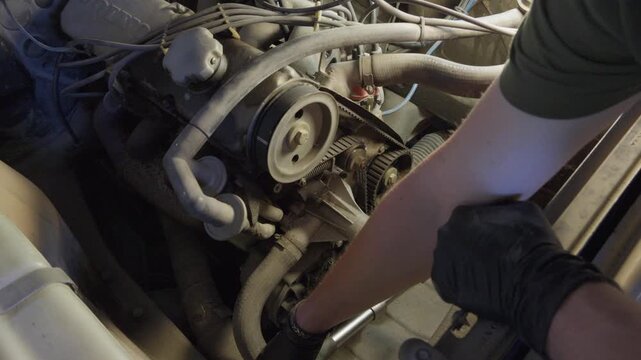 A mechanic manually rotates an old gasoline engine with a ratchet wrench during hands-on inspection and maintenance in the engine bay.