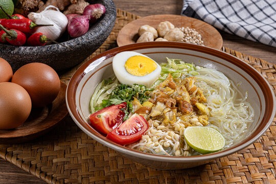 Authentic indonesian chicken soto soup bowl with glass noodles half egg tomatoes and raw traditional ingredients