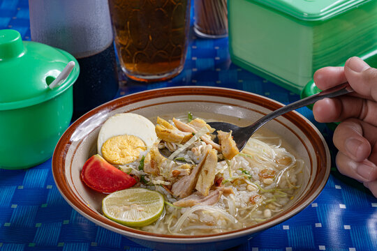 Hand scooping indonesian chicken soto soup with boiled egg served in a traditional indonesian warung setting