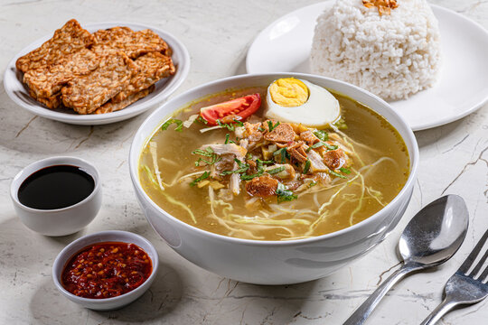 Indonesian chicken soto soup bowl with rice egg fried tempeh and sambal served in modern marble setting