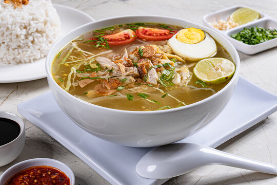 Indonesian chicken soto soup in white bowl with yellow broth egg tomato lime served in modern setting