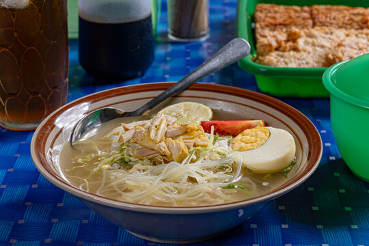 Indonesian chicken soto soup with glass noodles and egg served in a traditional indonesian warung setting