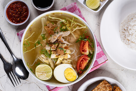 Overhead flat lay indonesian chicken soto soup with egg tomatoes rice pink checkered napkin modern marble setting