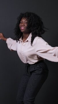 Cheerful and energetic african american businesswoman with curly hair dancing ecstatically in slow motion, celebrating a victory with happiness and excitement against a dark studio background
