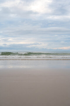 Low angle view of ocean waves breaking on a sandy beach under a cloudy sky.