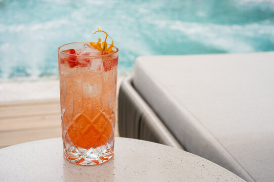 Tall glass of orange cocktail with flower garnish on a table by the pool.