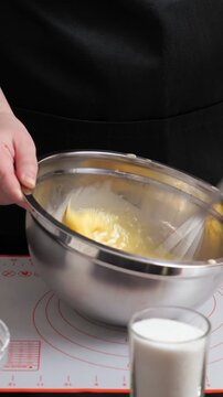 Close up shot of a pastry chef in a black apron meticulously whisking fresh eggs and milk in a shiny metal bowl, diligently preparing a smooth batter for a culinary creation