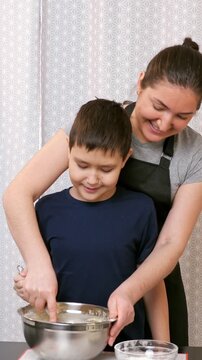 Loving mother teaching her young son to cook by guiding his hands as he whisks batter in a bowl, capturing a tender moment of family bonding, learning, and shared happiness