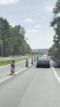 Car driving on a sunny city road with traffic cones and trees, showing lane work, travel, transport, and urban street safety in daylight.