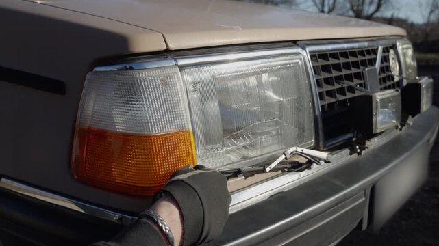 A mechanic removes the front light cover on an old car to access the bulb, showing practical automotive lighting repair at the vehicle's front end.
