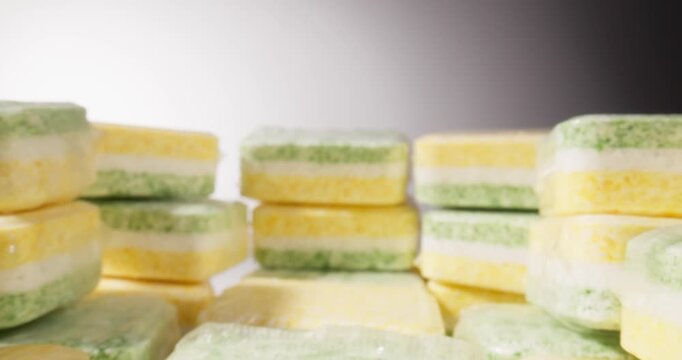 Stacked dishwasher tablets sliding across white studio table toward camera with shallow depth of field, probe lens.