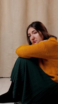 Melancholic young woman sitting alone on the floor, hugging her knees and looking down with a sorrowful expression, embodying feelings of depression, anxiety, and loneliness