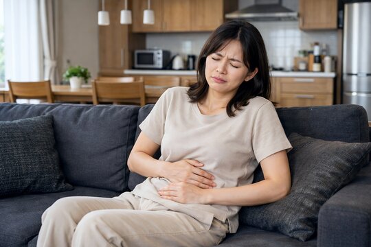 リビングのソファで腹痛に苦しむ女性お腹を押さえ体調不良を訴える