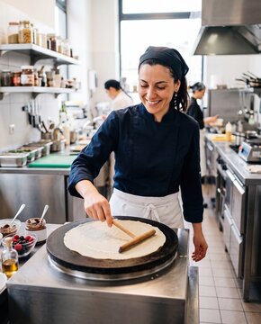Chef spreading crepe batter on hot plate, preparing dessert in commercial kitchen, cooking sweet food with berries