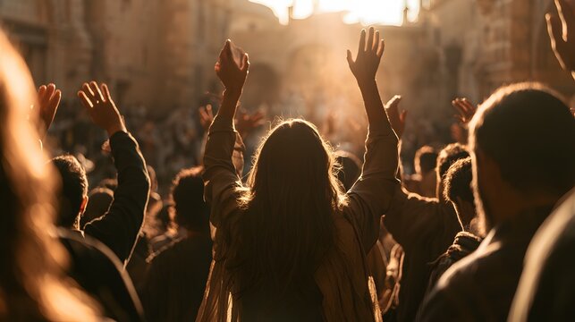 A large group of people with arms lifted in praise and worship at sunset in a public square