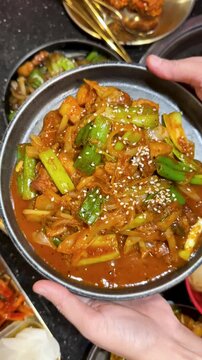 Hands Holding Plate of Spicy Korean Pork Stir Fry with Scallions