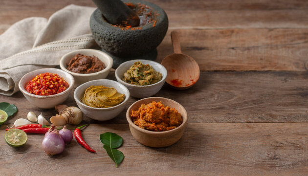 Assorted Thai curry pastes in small bowls with fresh ingredients on a rustic wooden table.