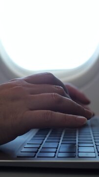 Close up of a businesswoman's hands typing on a modern laptop keyboard inside an airplane cabin, illustrating the concept of remote work and business travel while flying to a destination